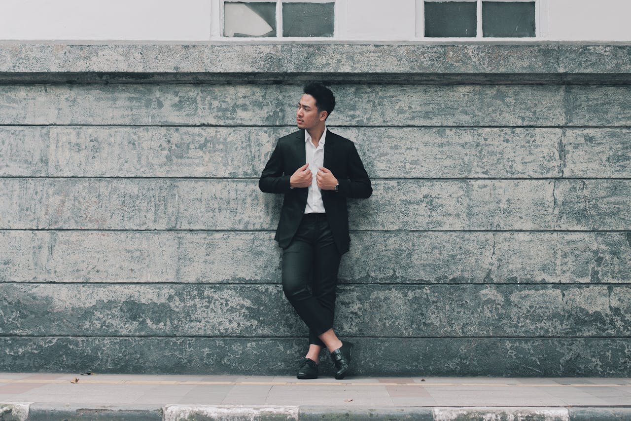 Mastering the First Impression: Your intriguing post title goes here Fashionable man in a suit leaning on city wall, exuding confidence and style.